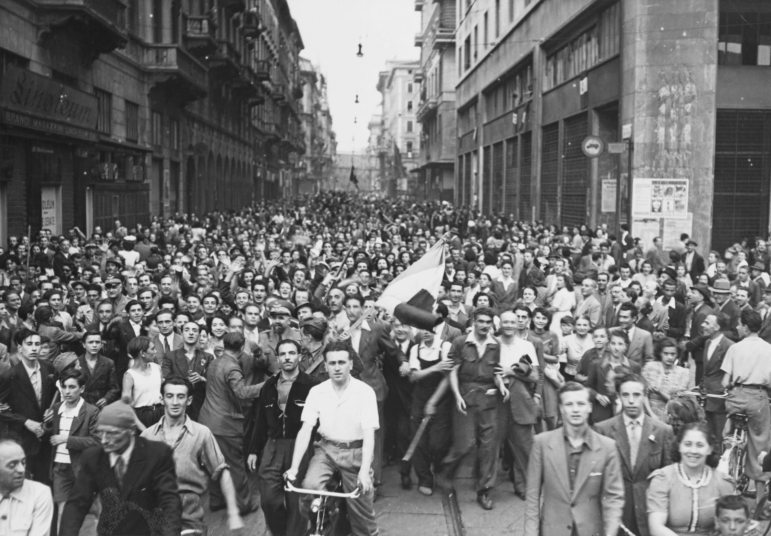 In this black-and-white photo, civilians fill the streets of Milan, Italy, on April 25, 1945, to celebrate their liberation by Italian partisans from German Nazi forces and the fascist regime.