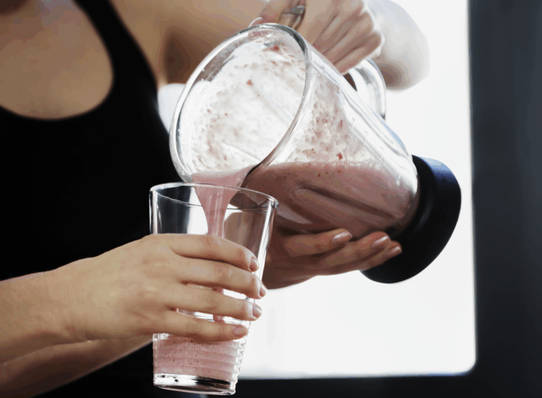 Close-up of woman pouring a meal replacement shake into her friend's glass. Horizontal shot.
