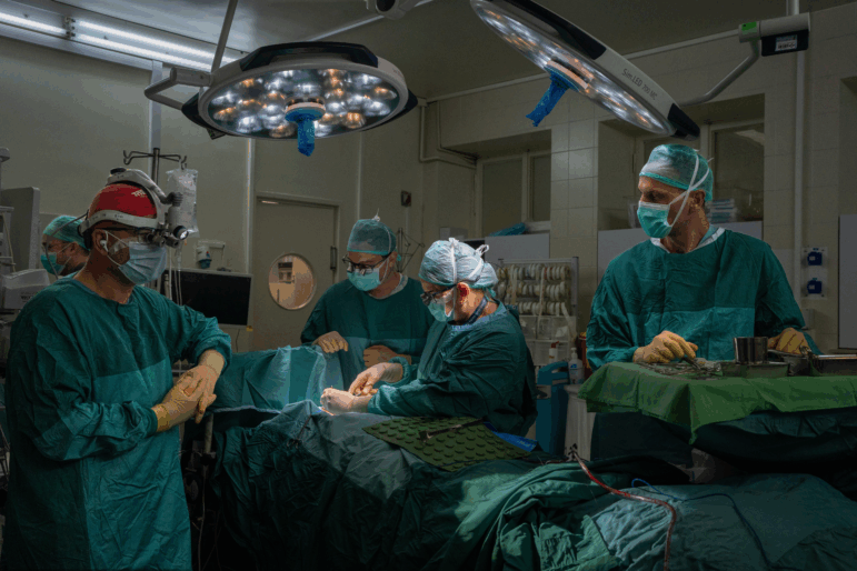 Medical workers surround a patient lying on a table in an operating room.