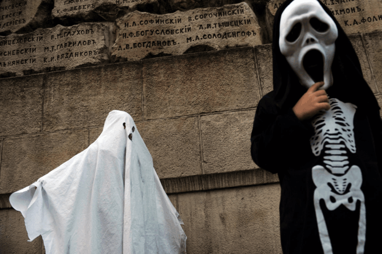 In this photo, the child on the left is draped in a white sheet as part of a ghost costume. The child on the right is dressed in a skeleton costume.