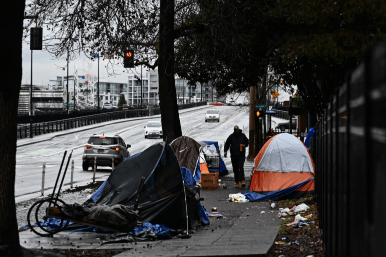 A pedestrian walks down a sidewalk in Portland, Oregon, that has tents on both sides of it.