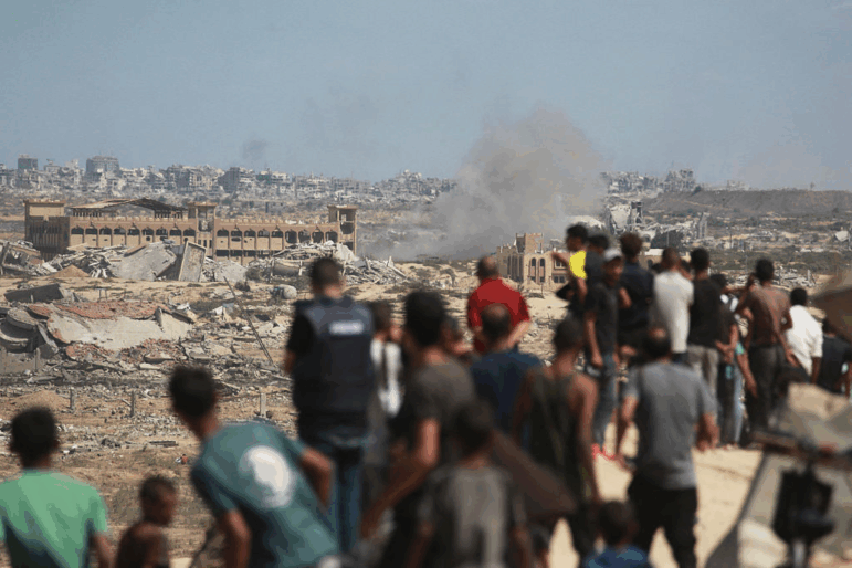 Palestinians watch smoke billowing during Israeli strikes upon arrival on a coastal path northwest of Nuseirat refugee camp.