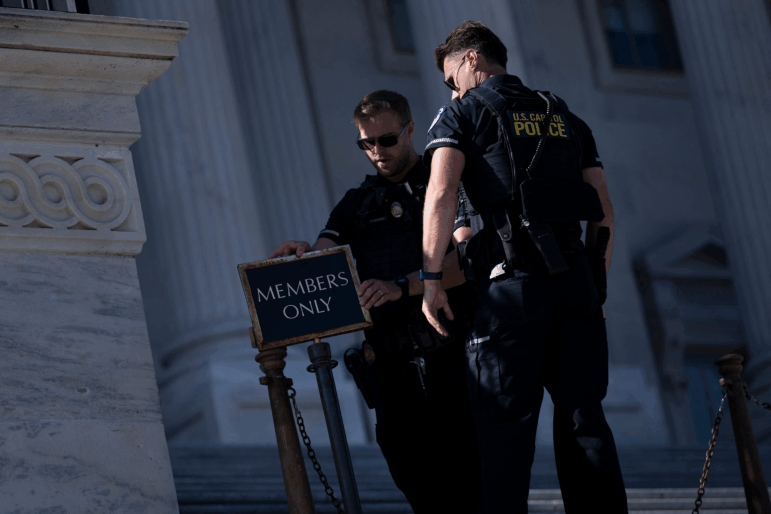 Standing outdoors, two U.S. Capitol Police officers close an entrance to the Capitol on October 9. One is setting up a sign on a post that says: "MEMBERS ONLY."