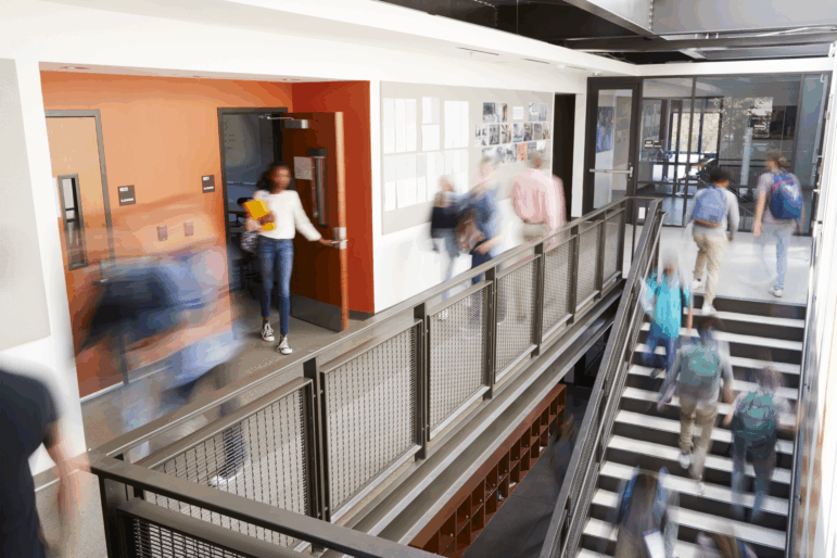 Busy high school corridor with blurred students and staff.