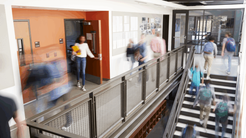 Busy high school corridor with blurred students and staff.