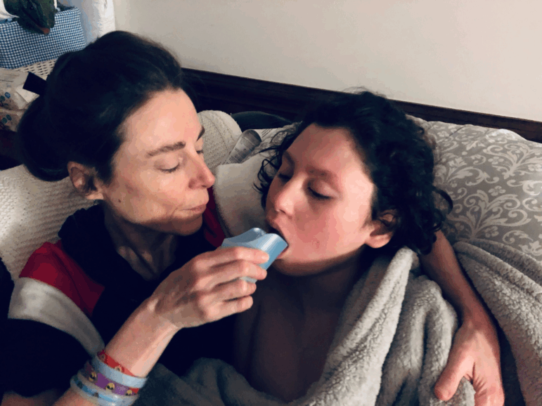 Alessandra Fabrello (left) holds a cup to the lips of her son Ysadore Maklakoff as he reclines and she hugs him.