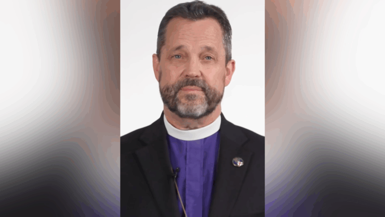 A screenshot of Archbishop Steve Wood wearing a blue shirt, white clerical collar and black blazer.