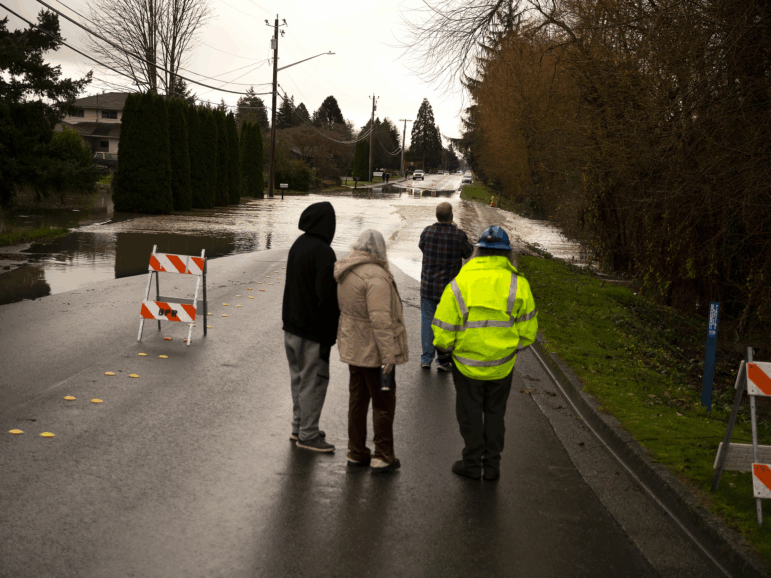 Neighbors watch as Gages Slough overflows and floods a street in Burlington, Wash., on Friday.