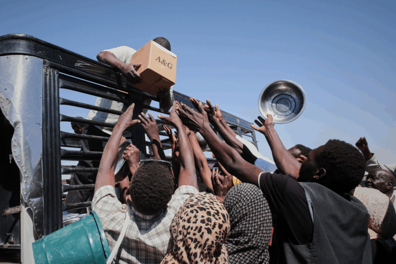Sudanese families displaced from El-Fasher reach out as aid workers distribute food supplies at the newly established El-Afadh camp in Al Dabbah, in Sudan's Northern State, Sunday, Nov. 16, 2025.