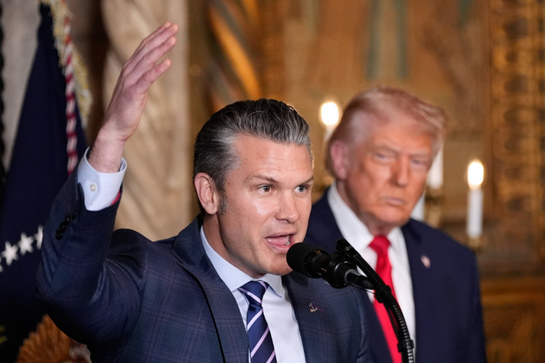 Defense Secretary Pete Hegseth speaks as President Donald Trump looks on, at Trump's Mar-a-Lago club, Monday, Dec. 22, 2025, in Palm Beach, Fla.