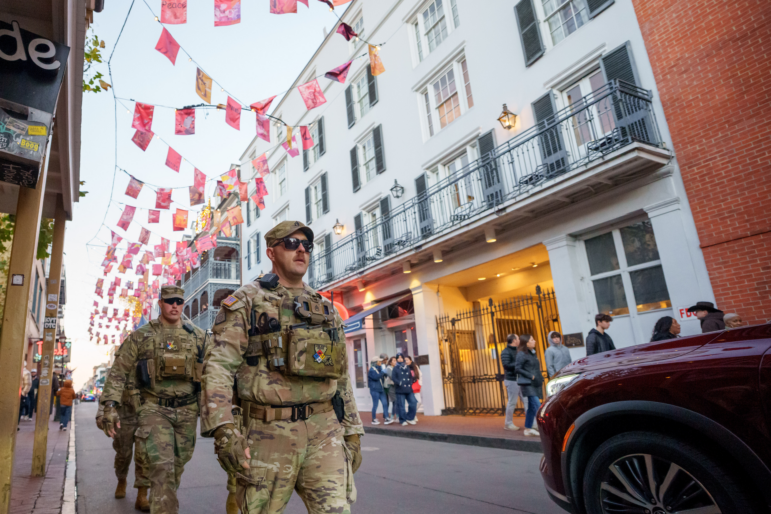 Walking under flags that memorialize victims of Jan. 1, 2025 attack, members of the Louisiana National Guard, military police, and Louisiana law enforcement agencies patrol the French Quarter along Bourbon Street and intersecting streets as part of a National Guard deployment for New Year's celebrations in New Orleans, Tuesday, Dec. 30, 2025. (AP Photo/Matthew Hinton)