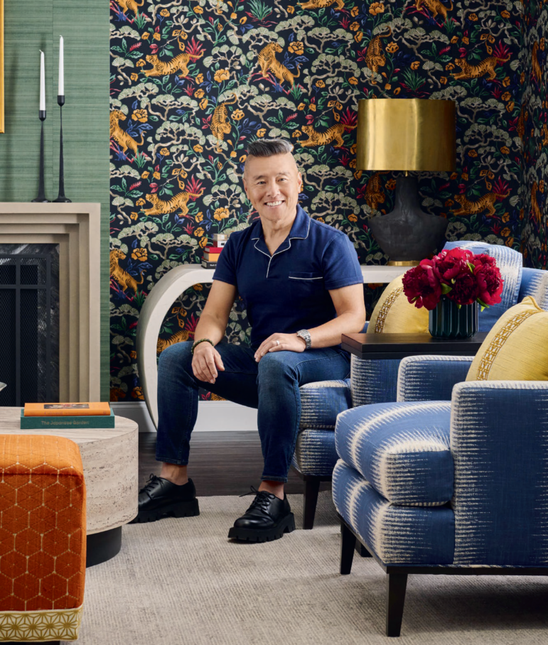 An environmental portrait of Vern Yip sitting on a blue and white patterned couch an aesthetically-pleasing living room he decorated, with tiger and floral patterned wallpaper behind him.