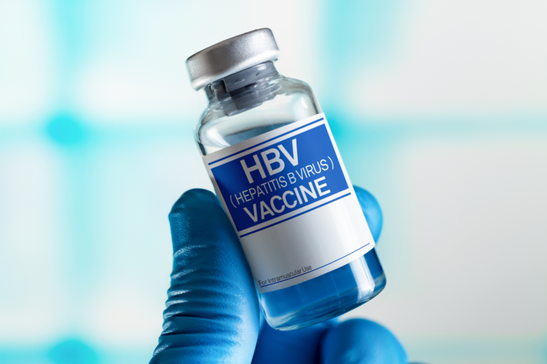 This photo shows a vial that's labeled "HBV (Hepatitis B Virus) Vaccine." A hand wearing a blue medical glove is holding the vial.