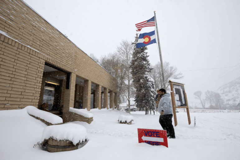 A voter carries his son as he walks into the Oak Creek Town Hall to drop off his ballot on Election Day, Nov. 5, 2024, in Oak Creek, Colo.