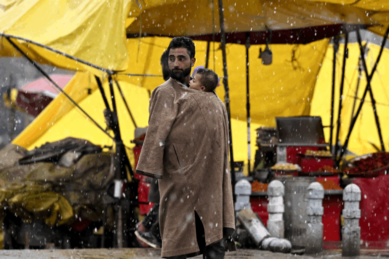 A man carries a child in his Kashmiri pheran (a traditional attire) amid snowfall in Srinagar on February 27, 2025.