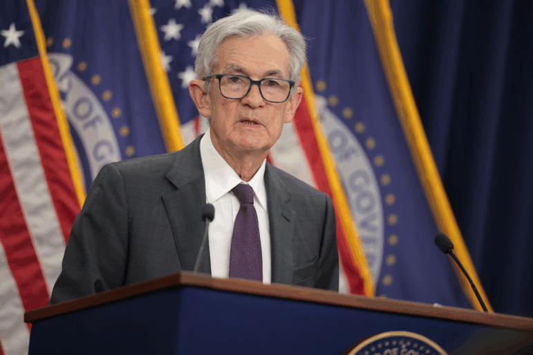Federal Reserve Chair Jerome Powell stands behind a lectern that has a microphone attached to it. He's wearing a suit and glasses.