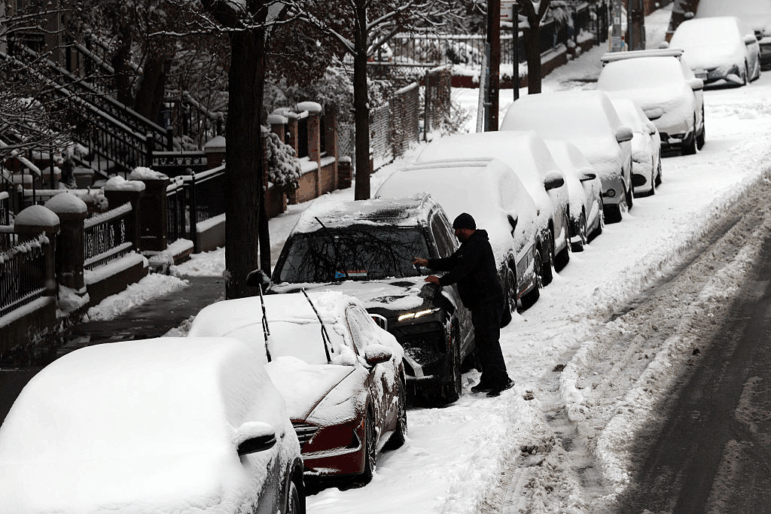 A man cleans off his car of snow in Brooklyn after an overnight storm on Dec. 27, 2025 in New York City.