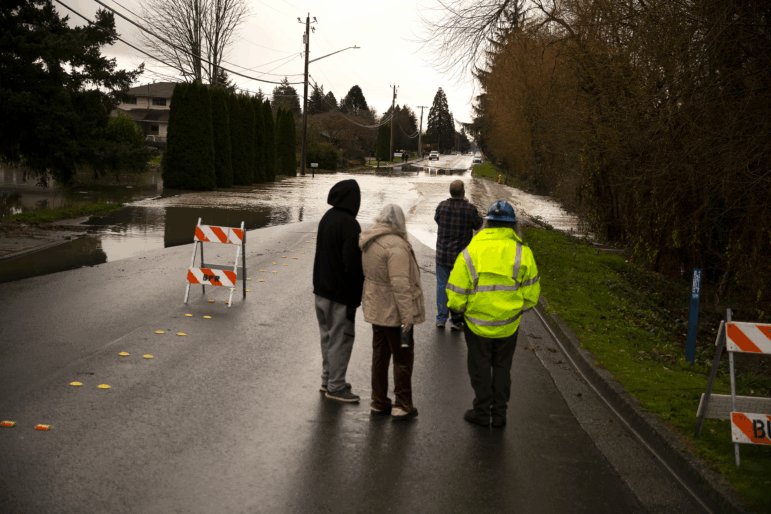 Neighbors watch as Gages Slough overflows and floods a street in Burlington, Wash., on Friday.