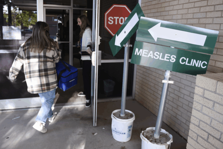 A sign that says "Measles Clinic" is shown. Two people are entering the Andrews County Health Department in Texas.