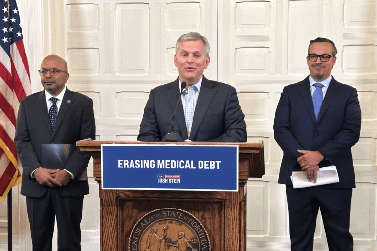 North Carolina Gov. Josh Stein, center, flanked by the state's health secretary, Dr. Dev Sangvai, left, and an executive from Undue Medical Debt, Jose Penabad, speaks about the elimination of medical debt through an initiative involving hospitals and Medicaid in Raleigh, N.C.