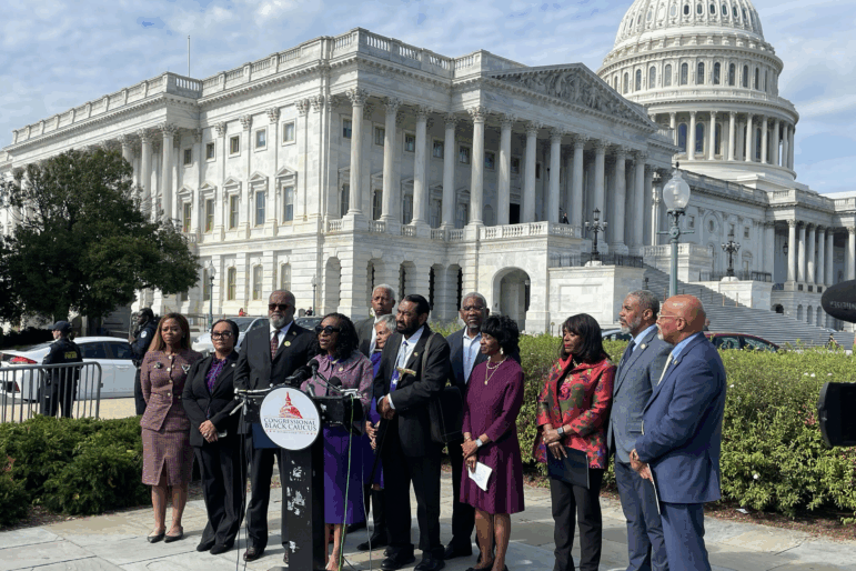 Members of the Congressional Black Caucus speak outside the U.S. Capitol in October. They are standing around a lectern that has microphones attached to it.