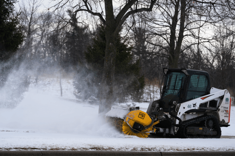 A plow clears snow from a snow-covered sidewalk during a cold day in Lake Forest, Ill., Wednesday, Jan. 21, 2026.