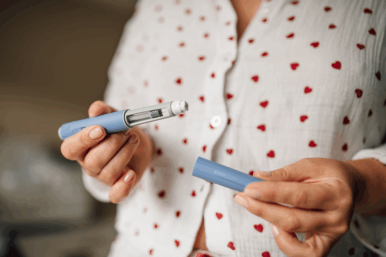 A woman in pajamas is shown holding an injection pen in front of her torso.
