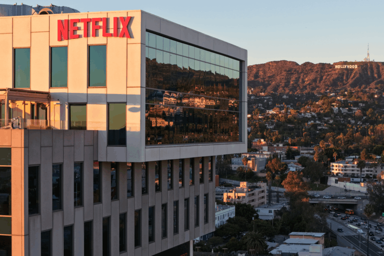 An aerial view of the Netflix logo displayed at Netflix studios, with the Hollywood sign in the distance.