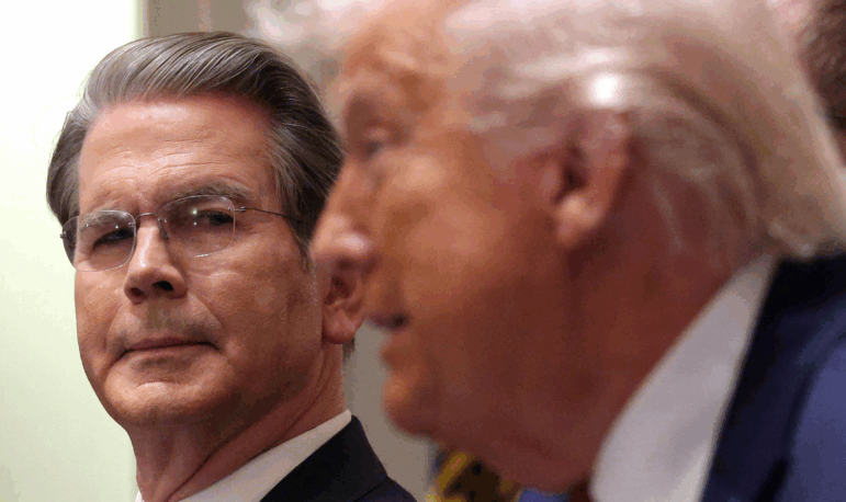 Photographed from the neck up, Treasury Secretary Scott Bessent is on the left side of the frame, looking in the direction of President Trump, who appears in profile on the right side of the frame.
