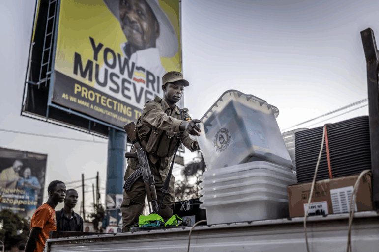 A Ugandan police officer unloads ballot boxes from a truck at a polling station set up in front of an electoral billboard supporting Uganda's incumbent president Yoweri Museveni in Kampala on Jan. 15, 2026.