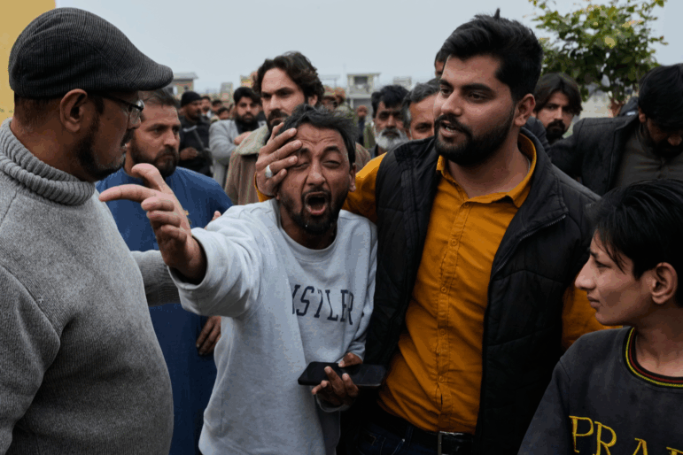People comfort a man, center, mourning over the death of his relative, close to the site of a bomb explosion at a Shiite mosque, in Islamabad, Pakistan.