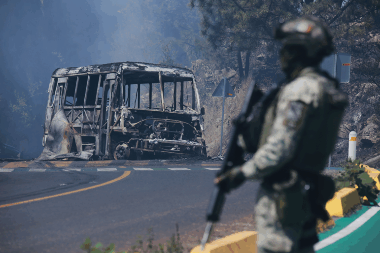 A soldier stands guard by a charred vehicle after it was set on fire, in Cointzio, Michoacán state, Mexico, Sunday, Feb. 22, 2026, following the death of the leader of the Jalisco New Generation Cartel, Nemesio Oseguera, known as "El Mencho."