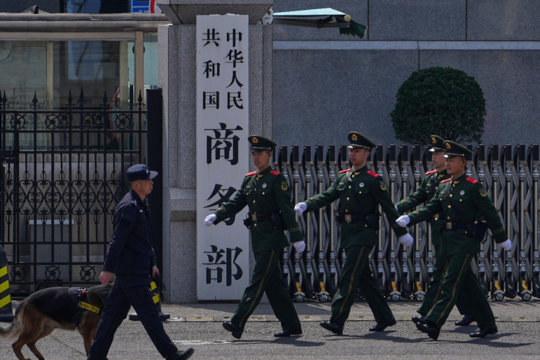FILE - Paramilitary soldiers and a police officer with a sniffer dog march past the main entrance gate of China's Ministry of Commerce, in Beijing, on April 3, 2025.