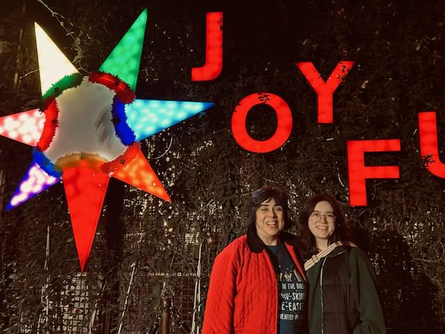Barbara Alvarez and her daughter, Monica Dreesen, stand next to one another. A large star decoration is on the backdrop behind them.