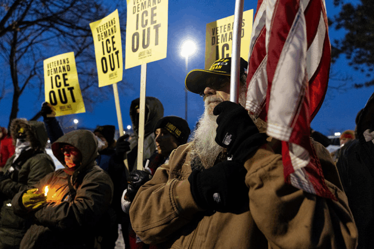 U.S. Navy veteran Earl Netwal, 77, holds a U.S. flag at a vigil while others near him hold signs that say "ICE out."