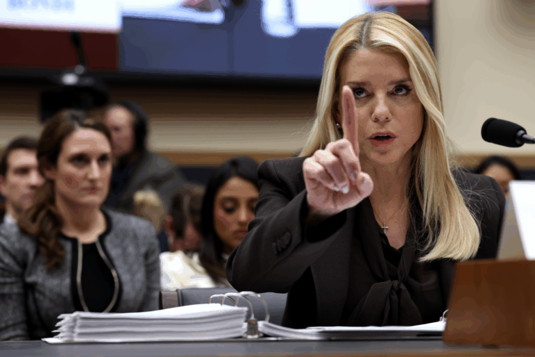 Seated behind a microphone, Attorney General Pam Bondi raises her index finger in the air while testifying before the House Judiciary Committee.