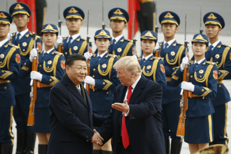 President Trump and Chinese President Xi Jinping shake hands at a welcoming ceremony on November 9, 2017, in Beijing. Two rows of military personnel wearing uniforms and carrying rifles with bayonets stand in the background.