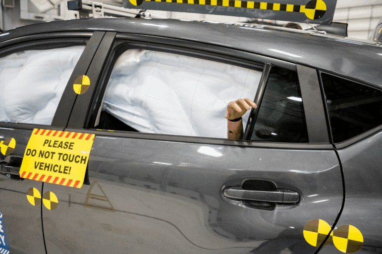 A crash-tested vehicle sits in the test hall, with airbags deployed and a crash test dummy's hand visible in the rear window, after a moderate overlap frontal crash test at the Insurance Institute for Highway Safety in Ruckersville, Va., on Tuesday, Dec. 2, 2025.