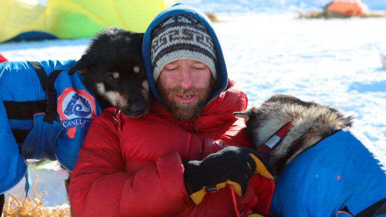 Musher Jessie Holmes takes a break from cooking his dogs a meal to nuzzle.