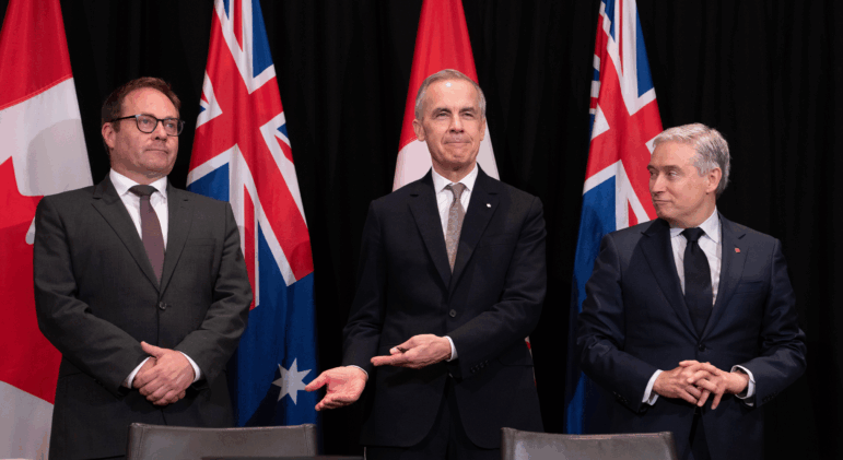 Canada's Prime Minister Mark Carney, center, gestures to Daniel Mulino, Australian Assistant Treasurer as he is introduced at the start of a signing ceremony, as Canada's Finance and National Revenue Minister Francois-Philippe Champagne, right, looks on, in Sydney, Australia, Wednesday, March 4, 2026. (Adrian Wyld/The Canadian Press via AP)