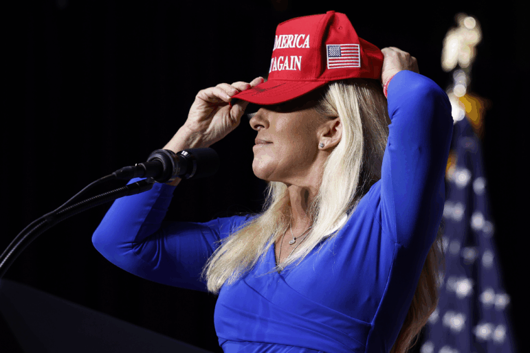 In this file photo, then-Rep. Marjorie Taylor Greene (R-GA) puts on her Make America Great Again hat while addressing a campaign rally with then Republican presidential candidate and former President Donald Trump March 9, 2024 in Rome, Georgia. After Trump ordered strikes on Iran March 1, 2026, Greene sharply criticized the president for abandoning "America First" foreign policy and his promises of "no new wars."