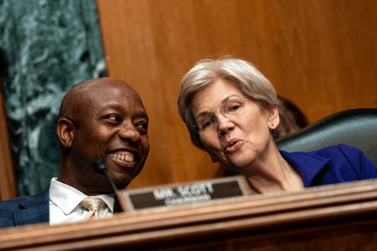Sen. Tim Scott, seated on the left side of the frame, chats with Sen. Elizabeth Warren, seated on the right side of the frame, during a hearing on Capitol Hill in June 2025.