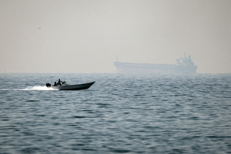 A motorboat cruises off the coast of the United Arab Emirates, on the Strait of Hormuz, with a tanker seen in the background, on February 25, 2026. Tanker traffic through the strait has come essentially to a stop after Iran declared the strait closed following attacks on Iran by the U.S. and Israel.