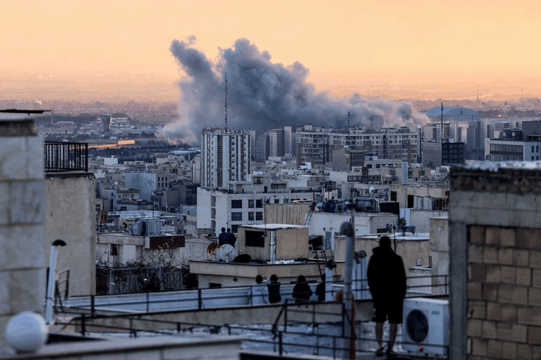 A person stands on the roof of a building looking at a plume of smoke rises after a strike on the Iranian capital Tehran, on March 3, 2026.