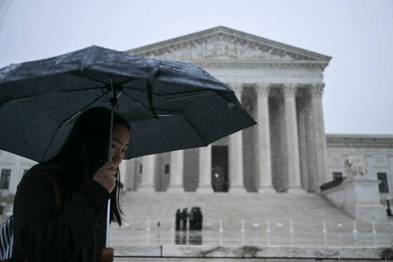 Snow flurries fall as a woman carries an umbrella near the US Supreme Court in Washington, DC, on March 12, 2026. Following record high temperatures the day before, Washington, DC, recieved snow flurries on Thursday.